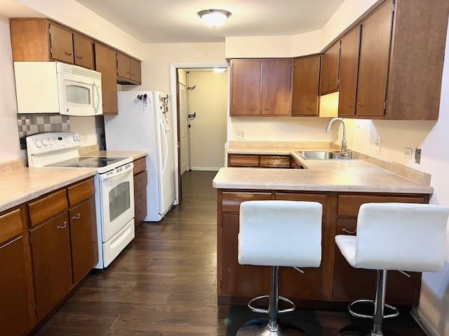 kitchen with a breakfast bar, dark wood finished floors, light countertops, a sink, and white appliances