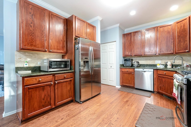 kitchen featuring sink, tasteful backsplash, light wood-type flooring, ornamental molding, and appliances with stainless steel finishes