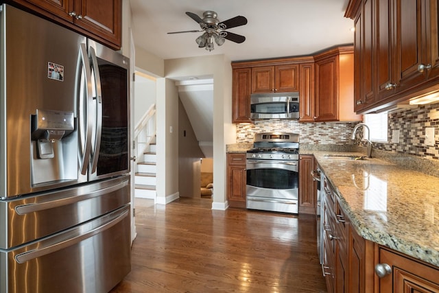 kitchen with sink, dark wood-type flooring, stainless steel appliances, light stone counters, and tasteful backsplash