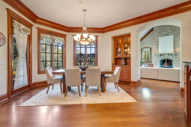 dining space with an inviting chandelier, ornamental molding, a stone fireplace, and hardwood / wood-style floors