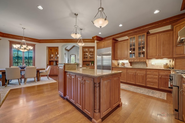 kitchen with a kitchen island with sink, light stone counters, decorative light fixtures, and stainless steel appliances