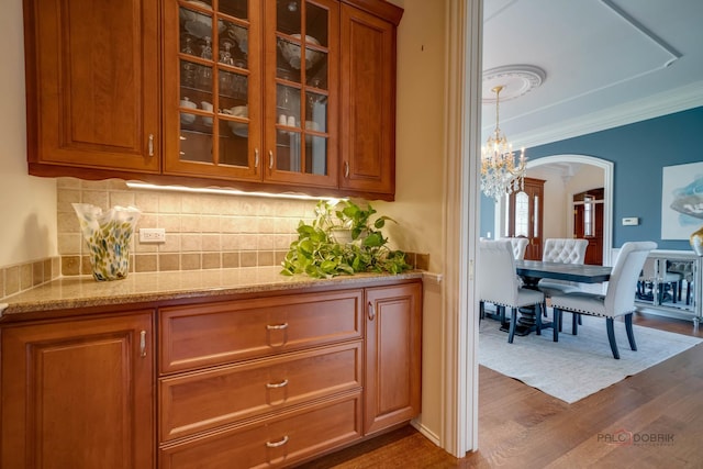 bar featuring decorative backsplash, ornamental molding, light stone countertops, dark wood-type flooring, and an inviting chandelier