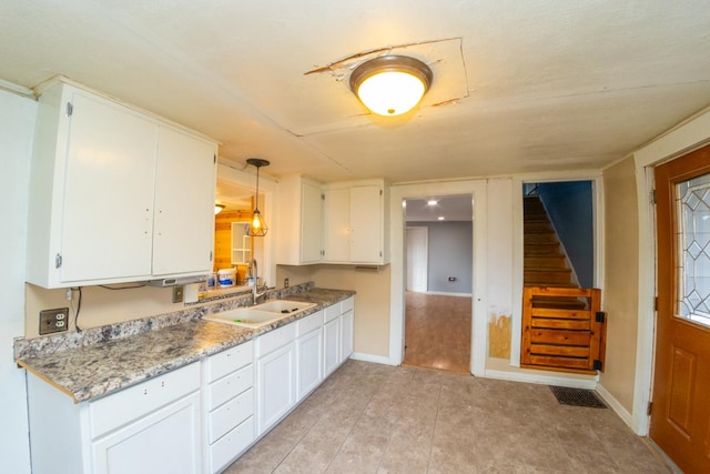 kitchen featuring sink, light tile patterned floors, white cabinetry, light stone countertops, and decorative light fixtures