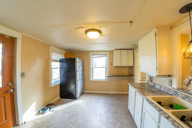 kitchen featuring sink, pendant lighting, white cabinets, and stainless steel refrigerator