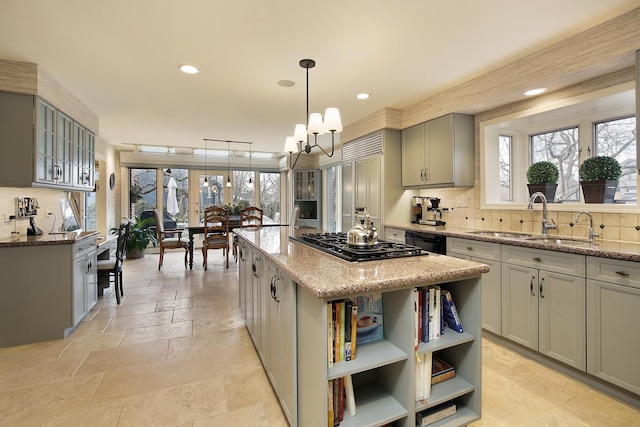 kitchen featuring sink, hanging light fixtures, a center island, light stone countertops, and stainless steel gas cooktop