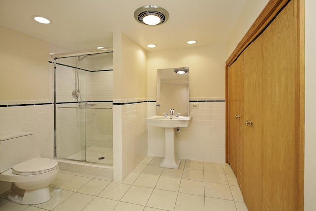 bathroom with tile patterned flooring, a shower with door, toilet, and tile walls