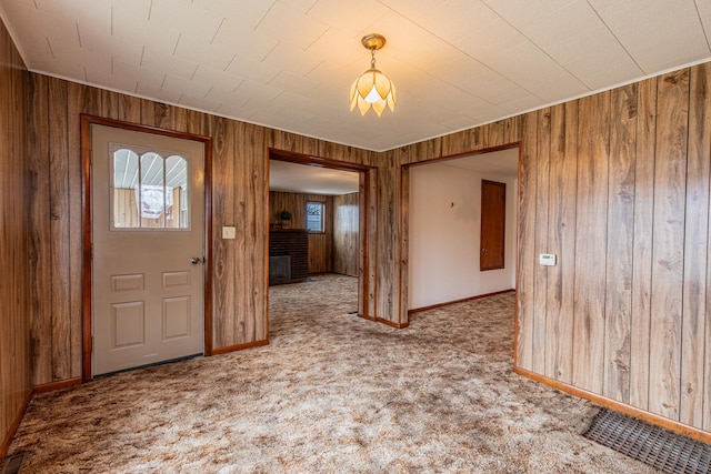 foyer with a brick fireplace, carpet flooring, and wood walls