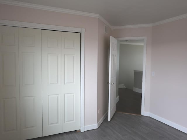 unfurnished bedroom with dark wood-type flooring, ornamental molding, and a closet