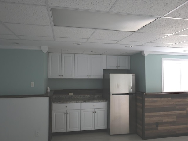 kitchen with a drop ceiling, white cabinets, and stainless steel refrigerator