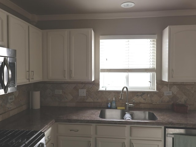 kitchen featuring appliances with stainless steel finishes, white cabinetry, sink, backsplash, and ornamental molding