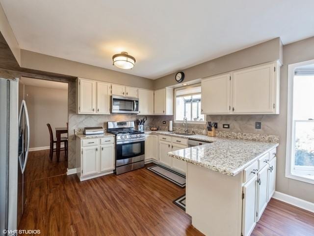 kitchen with appliances with stainless steel finishes, backsplash, light stone countertops, white cabinets, and kitchen peninsula