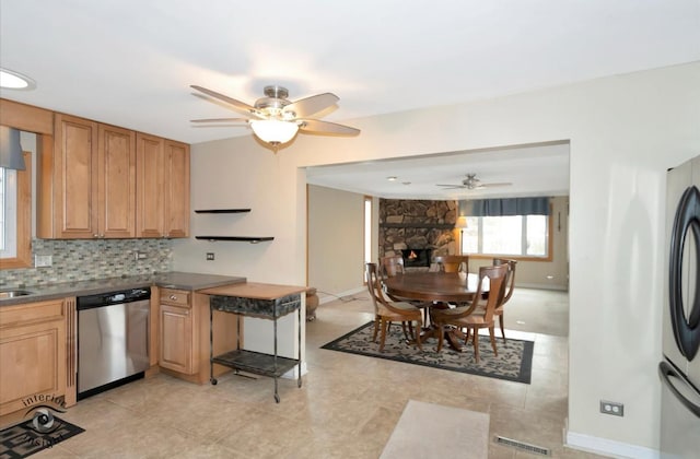 kitchen with ceiling fan, appliances with stainless steel finishes, a fireplace, and decorative backsplash