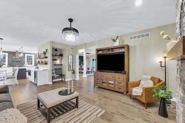 living area featuring visible vents, a fireplace, light wood-type flooring, and an inviting chandelier