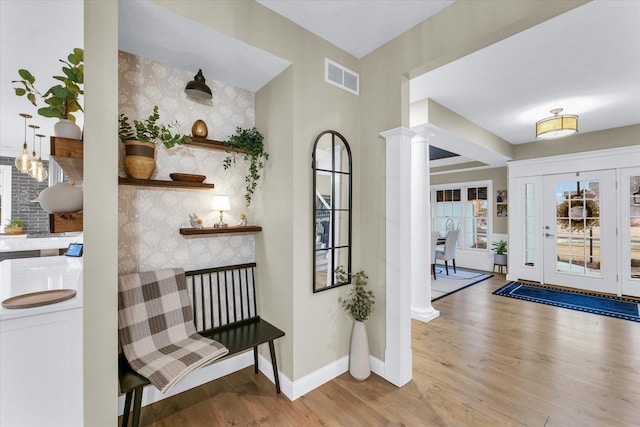 foyer entrance with visible vents, wood finished floors, wallpapered walls, baseboards, and ornate columns