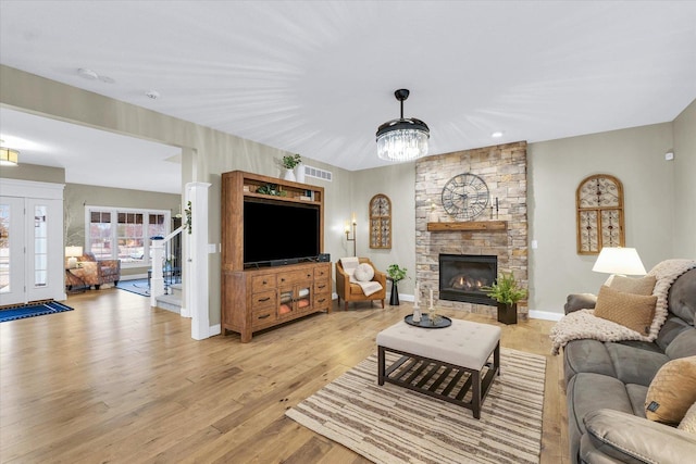 living room with visible vents, light wood-style floors, a stone fireplace, baseboards, and stairs