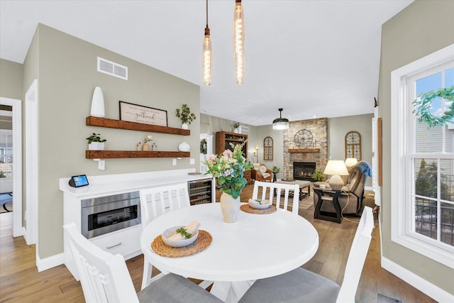 dining room with visible vents, beverage cooler, a stone fireplace, light wood finished floors, and baseboards