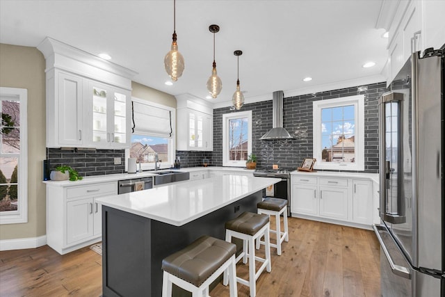 kitchen with tasteful backsplash, appliances with stainless steel finishes, a breakfast bar area, wall chimney exhaust hood, and white cabinets