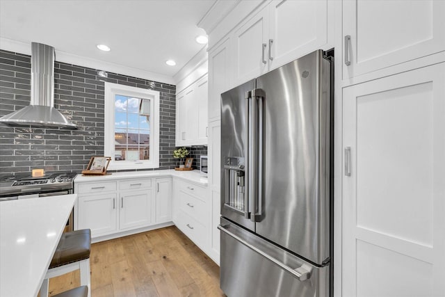 kitchen with stainless steel appliances, white cabinetry, tasteful backsplash, and wall chimney range hood