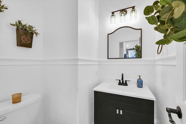 half bathroom with wainscoting, toilet, and vanity