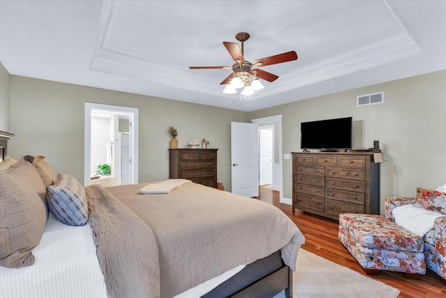 bedroom featuring ceiling fan, visible vents, a raised ceiling, and wood finished floors