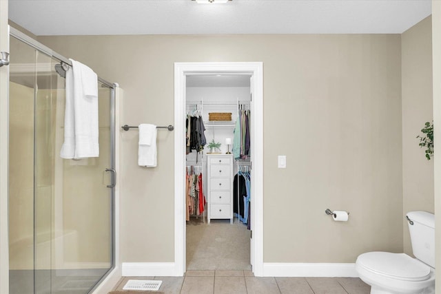 full bath with toilet, a spacious closet, a shower stall, and tile patterned flooring