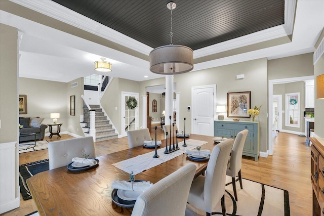 dining space featuring visible vents, a tray ceiling, stairway, light wood-style floors, and crown molding