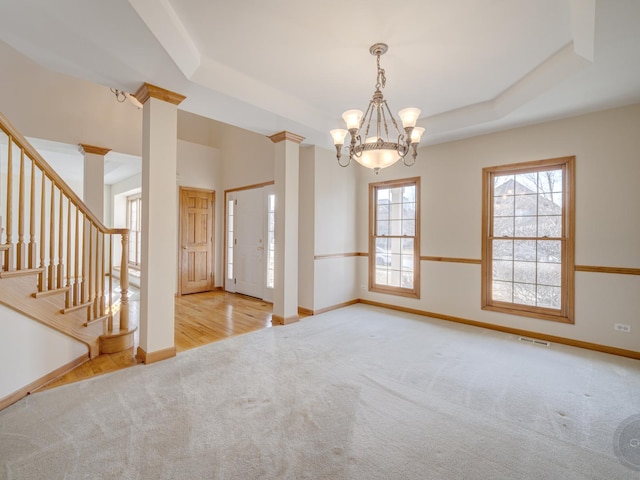 carpeted spare room with decorative columns, a chandelier, and a tray ceiling