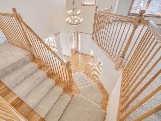 stairs featuring an inviting chandelier, a towering ceiling, and wood-type flooring