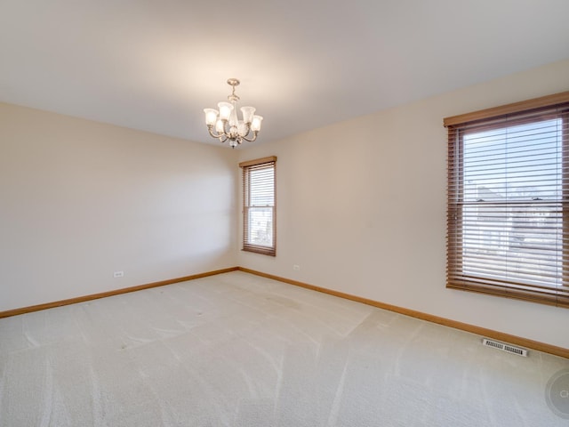 carpeted spare room featuring an inviting chandelier