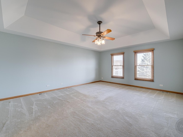 empty room featuring light colored carpet, a raised ceiling, and ceiling fan