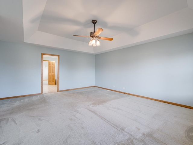 spare room featuring a tray ceiling, light colored carpet, and ceiling fan