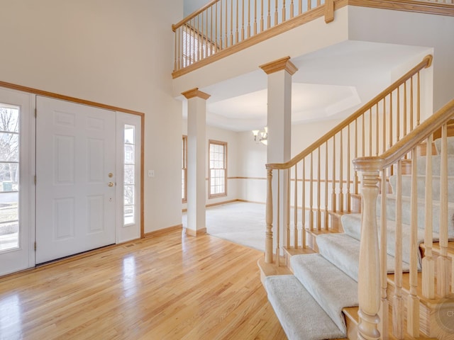 entryway with decorative columns, a high ceiling, an inviting chandelier, and light hardwood / wood-style floors