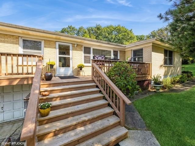 doorway to property with a wooden deck, brick siding, a garage, and a lawn