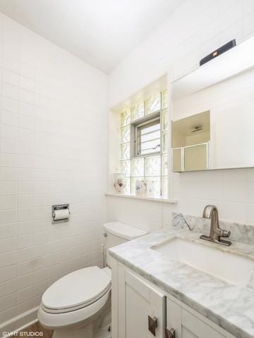 bathroom featuring toilet, tile walls, and vanity