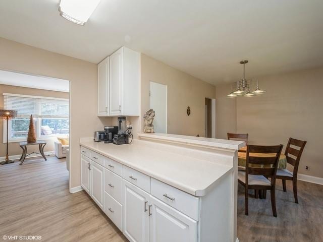 kitchen with a chandelier, light wood-style flooring, white cabinets, and a peninsula