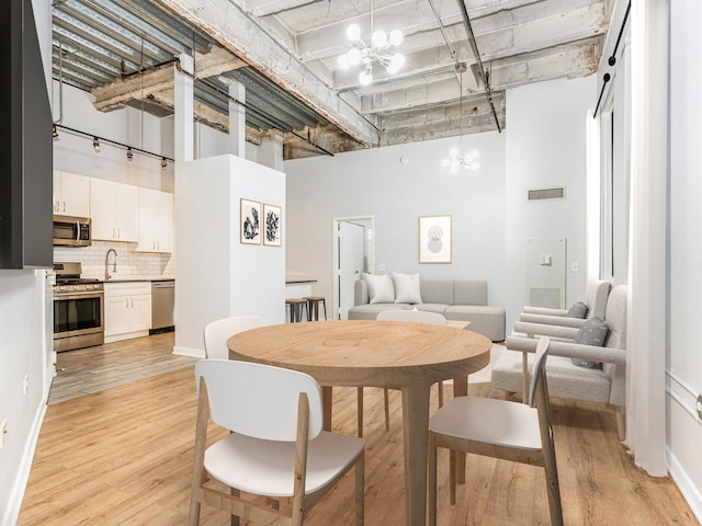 dining space with a towering ceiling, a chandelier, and light wood-type flooring