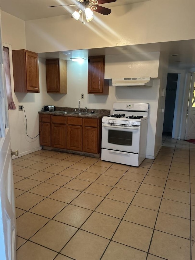 kitchen with white gas range, sink, light tile patterned floors, and ceiling fan