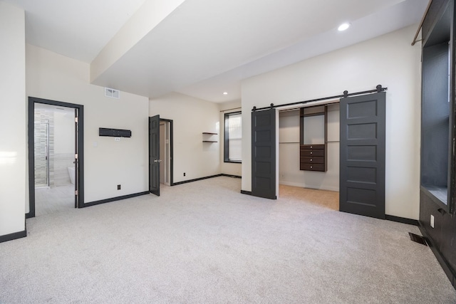 unfurnished bedroom with a barn door and light carpet