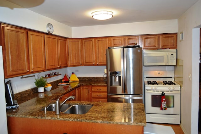 kitchen with brown cabinetry, a peninsula, a sink, and white appliances