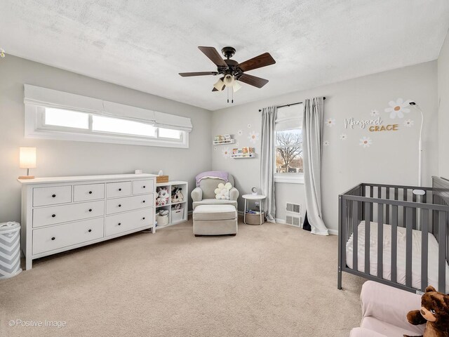 carpeted bedroom featuring ceiling fan, a textured ceiling, and a crib