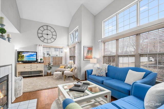 living room with a tiled fireplace, light hardwood / wood-style flooring, and high vaulted ceiling