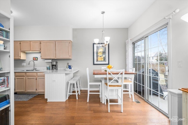 kitchen featuring light brown cabinetry, sink, a chandelier, hanging light fixtures, and hardwood / wood-style flooring