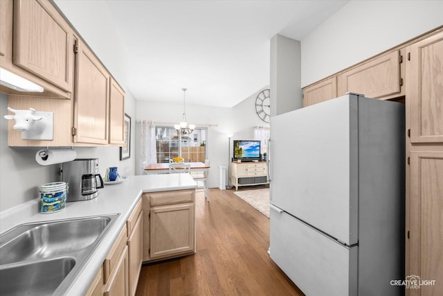 kitchen with light brown cabinetry, sink, decorative light fixtures, white fridge, and light hardwood / wood-style floors