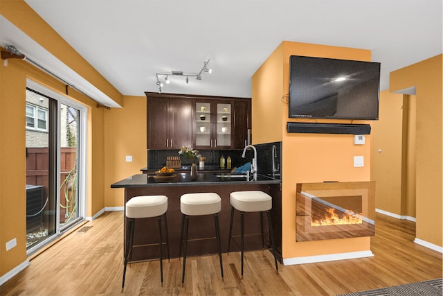 kitchen with dark brown cabinetry, sink, tasteful backsplash, light wood-type flooring, and kitchen peninsula