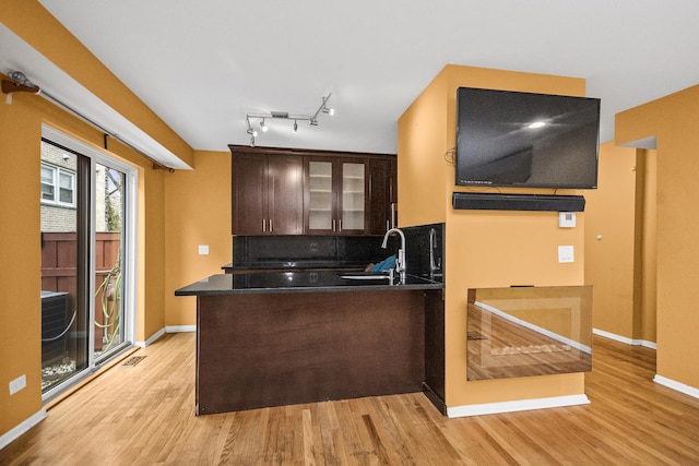 kitchen with sink, dark brown cabinets, light hardwood / wood-style flooring, kitchen peninsula, and decorative backsplash