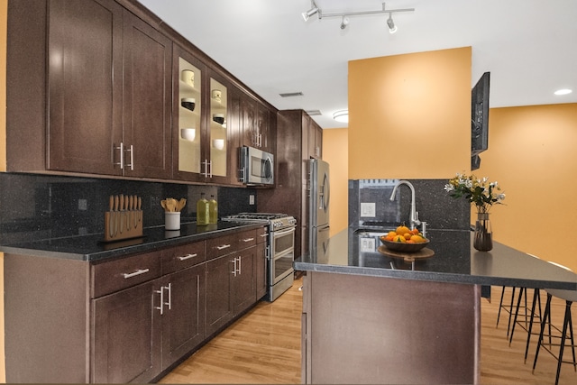 kitchen featuring appliances with stainless steel finishes, sink, backsplash, a kitchen breakfast bar, and light wood-type flooring