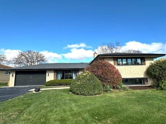 view of front of property with brick siding, a front lawn, aphalt driveway, a chimney, and an attached garage