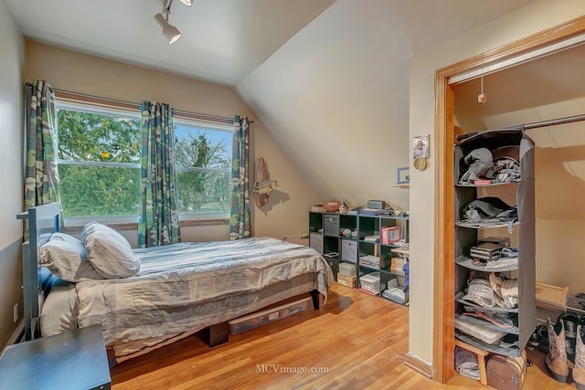 bedroom featuring hardwood / wood-style flooring, lofted ceiling, and rail lighting