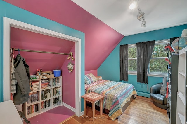 bedroom featuring vaulted ceiling, track lighting, baseboard heating, and light wood-type flooring