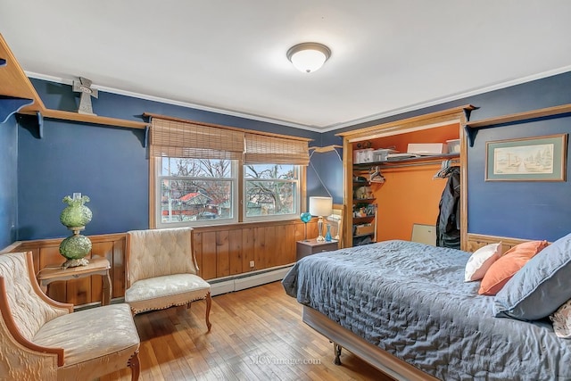 bedroom featuring crown molding, hardwood / wood-style floors, a spacious closet, a baseboard radiator, and a closet